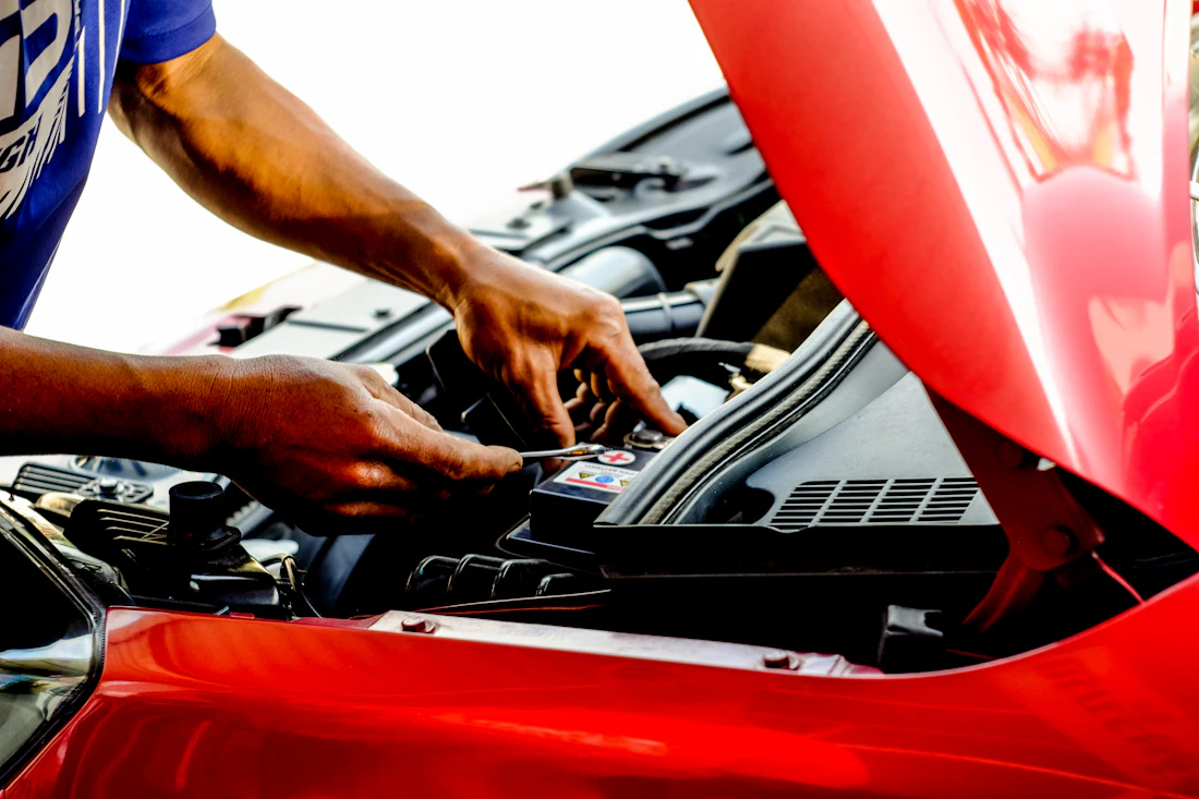 Technician's hands working in the engine bay of a red car