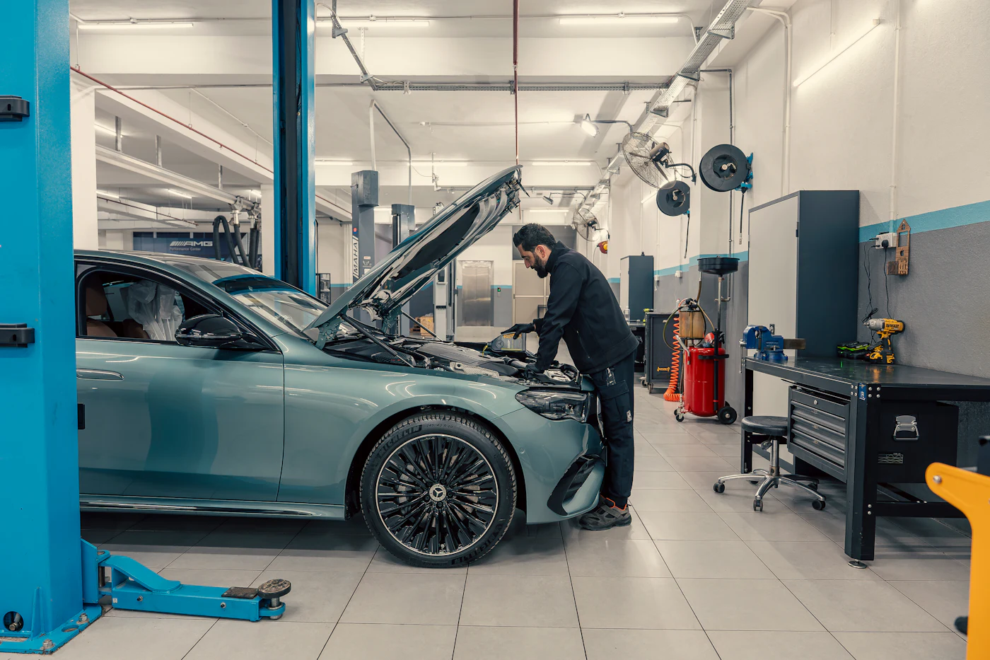 Technician working under the bonnet of a car in a bright, modern workshop
